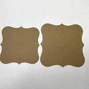 May include: Two brown paper tags with scalloped edges. The tags are blank and ready to be written on.
