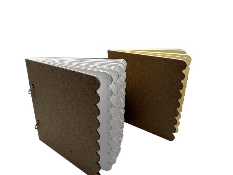 Puede incluir: Dos cuadernos peque&ntilde;os hechos a mano. Las cubiertas son marrones con un borde festoneado. Las p&aacute;ginas son blancas y beige, y los libros se sujetan con anillas met&aacute;licas. Sobre un fondo blanco.