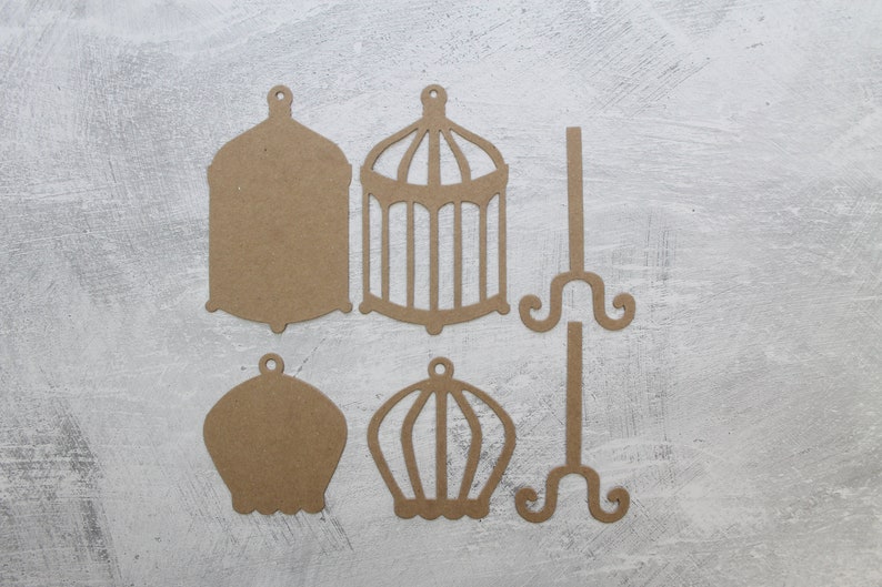 May include: Five brown paper cutouts of birdcages and stands. Two of the birdcages are solid, while the other three have a cut-out design. One of the stands has a cut-out design.