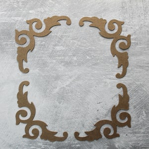 May include: Four brown paper cutouts in the shape of ornate corners form a square frame on a gray background.