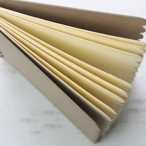 K&ouml;nnte beinhalten: Ein braunes Spiralblock mit cremefarbenen Seiten. Das Notizbuch ist ge&ouml;ffnet und die Seiten sind aufgef&auml;chert.