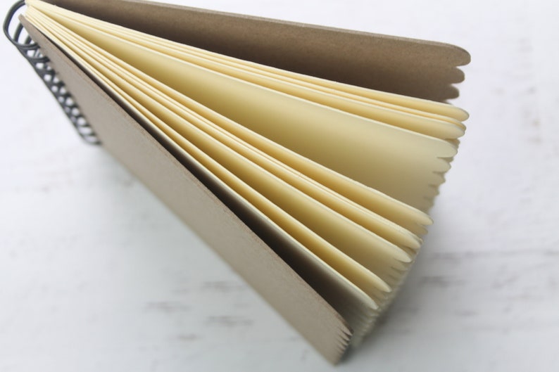 K&ouml;nnte beinhalten: Ein braunes Spiralblock mit cremefarbenen Seiten. Das Notizbuch ist ge&ouml;ffnet und die Seiten sind aufgef&auml;chert.