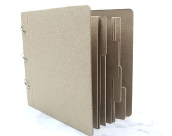 May include: A brown cardboard scrapbook with metal rings and dividers. The scrapbook is closed and the dividers are visible on the right side.