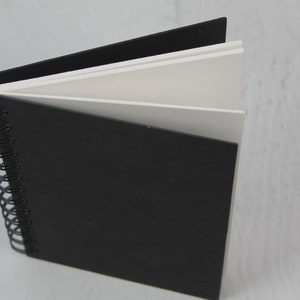 May include: A black spiral bound notebook with white paper inside. The notebook is closed and the cover is facing the camera.