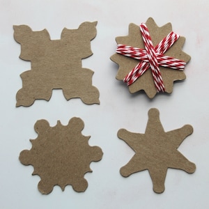 May include: Four brown paper gift tags with different shapes, including a square, a snowflake, a star, and a circle. The circle tag is wrapped with red and white twine.