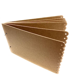 May include: A brown cardboard scrapbook with a scalloped edge and metal rings. The book is open to reveal blank pages.