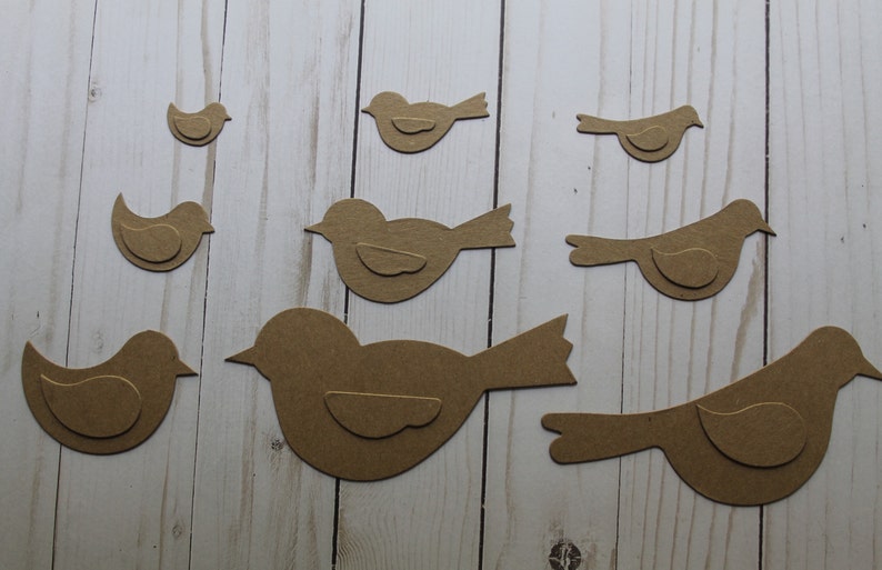 May include: A set of eight brown paper bird cutouts of varying sizes. The birds are all facing the right and have a simple design.