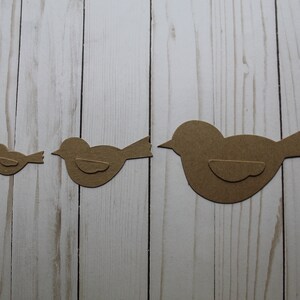 May include: Three brown paper bird cutouts of varying sizes. The birds are arranged in a row from smallest to largest.