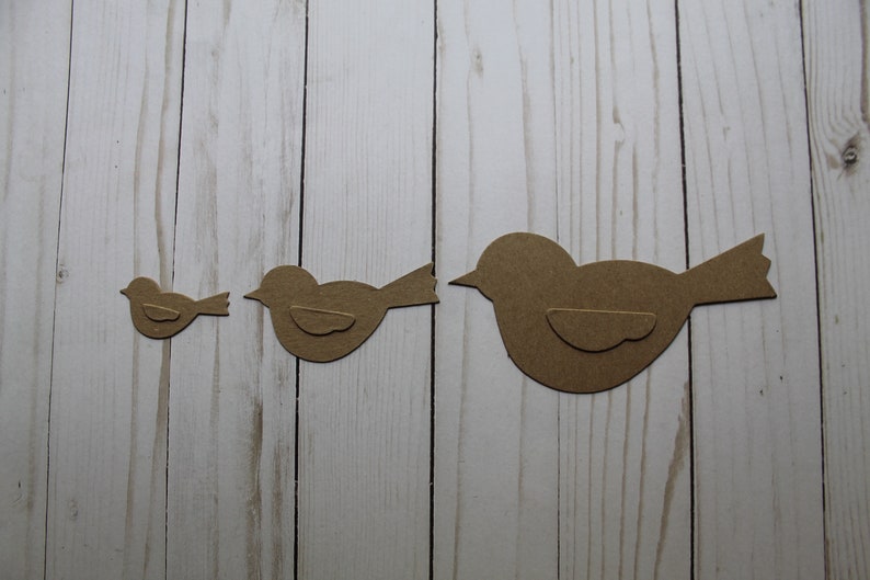 May include: Three brown paper bird cutouts of varying sizes. The birds are arranged in a row from smallest to largest.