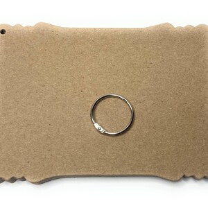 May include: A brown, rectangular, wooden sign with a decorative border and a hole at the top. A silver key ring is included.