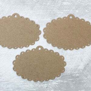 May include: Three brown oval-shaped paper tags with scalloped edges and a hole at the top. The tags are on a white textured background.