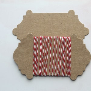 May include: Two brown paper gift tags with scalloped edges. The top tag is blank. The bottom tag has a spool of red and white baker's twine.