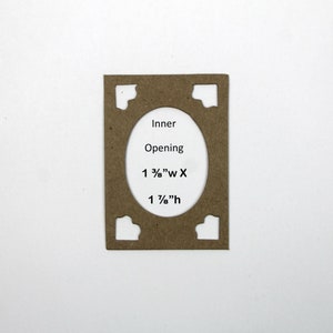 May include: A brown cardboard frame with a cut-out oval opening. The text "Inner Opening 1 3/8" W X 1 1/8" H" is printed on the frame.