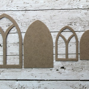 May include: Four unfinished wooden window cutouts in varying sizes. Two have arched tops with detailed tracery, while the others are solid arched shapes. The cutouts are arranged on a distressed white wooden surface.