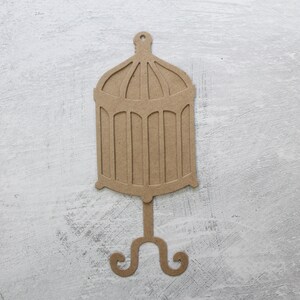 May include: A brown cardboard cutout of a birdcage with a decorative stand. The cage has a domed top and a round base.