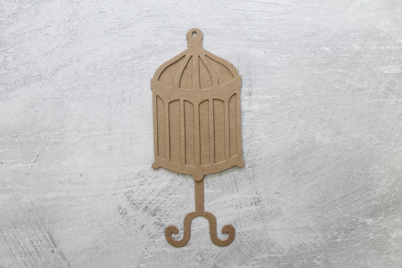 May include: A brown cardboard cutout of a birdcage with a decorative stand. The cage has a domed top and a round base.
