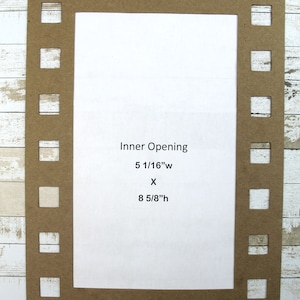 May include: A brown cardboard frame with a filmstrip border. The frame has an inner opening measuring 5 1/16 inches wide by 8 5/8 inches high. The frame is on a white wood background.