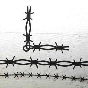 May include: Black barbed wire cutouts in various lengths and configurations. One piece forms a corner, while others are straight or shorter. The cutouts are arranged on a white, textured surface.