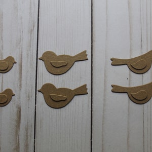 May include: Four brown paper bird cutouts on a white wood background. The birds are different sizes and are arranged in two rows of two.