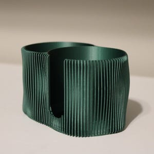 Può includere: Un organizer da scrivania verde scuro, stampato in 3D, con una texture a coste unica. L'organizer ha due scomparti circolari e una fessura centrale. Il design è moderno e minimalista, adatto per contenere penne, matite o piccoli accessori per l'ufficio.