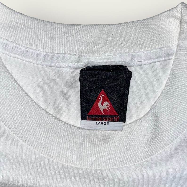 May include: White t-shirt with a black and red Le Coq Sportif tag that says "Large".
