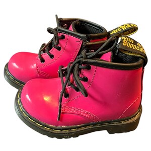 May include: Pink patent leather children's boots with black laces and a yellow "AirWair with Bouncing Soles" tag.