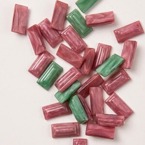 May include: A pile of pink and green rectangular buttons with a raised design. The buttons are made of a translucent material and have a marbled appearance.