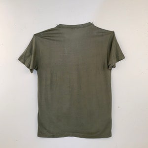 May include: Olive green t-shirt with short sleeves. The shirt is made of a thin, lightweight material and has a crew neck. The shirt is displayed against a white background.