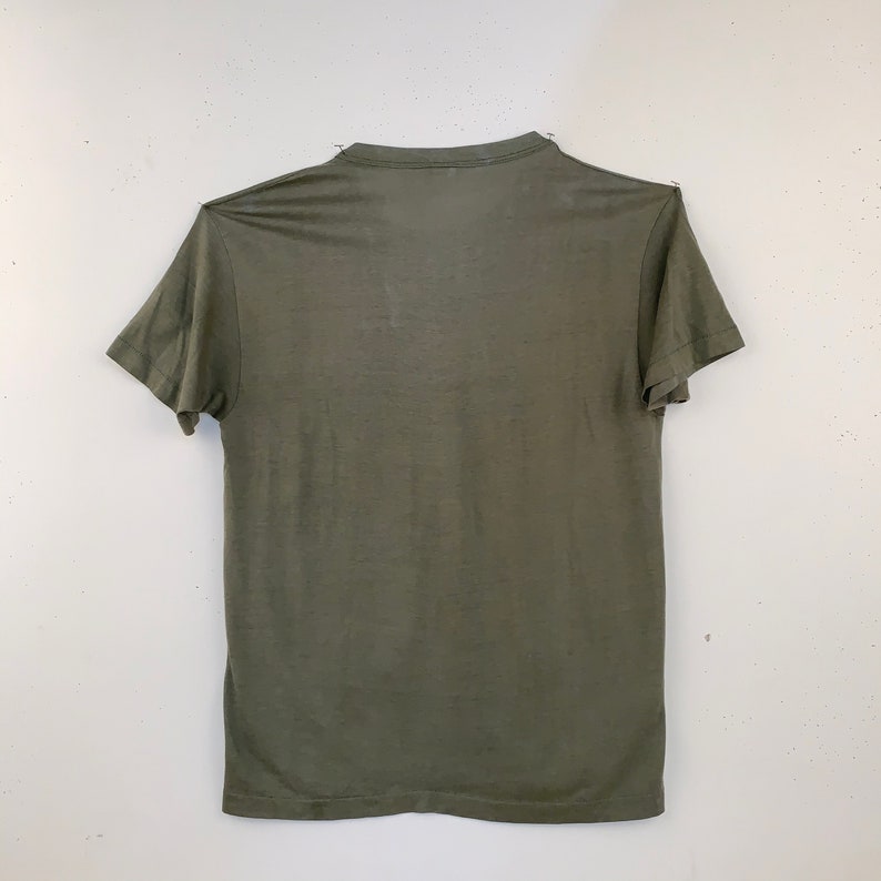 May include: Olive green t-shirt with short sleeves. The shirt is made of a thin, lightweight material and has a crew neck. The shirt is displayed against a white background.