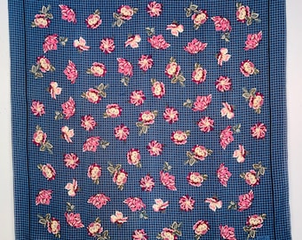 May include: A blue and white checkered fabric with a repeating pattern of pink flowers. The fabric has a black border.