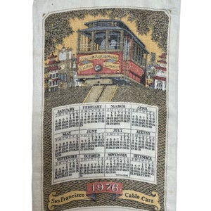 May include: A vintage 1976 calendar tea towel featuring a red and yellow cable car traveling up a hill in San Francisco. The calendar includes all 12 months of the year.