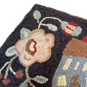 Pu&ograve; includere: Primo piano di un tappeto fatto a mano con un motivo floreale. Il tappeto presenta un grande fiore rosa con accenti marroni e gialli, circondato da fiori e foglie pi&ugrave; piccoli. Lo sfondo &egrave; di colore marrone scuro.
