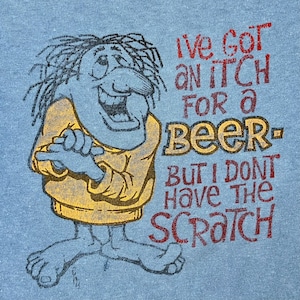 May include: A blue t-shirt with a cartoon character and the text "I've got an itch for a beer - but I don't have the scratch".