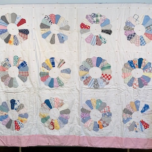 May include: A vintage quilt with a white background and pink border. The quilt is made up of 12 circular patchwork designs, each with a different pattern of colorful fabric.