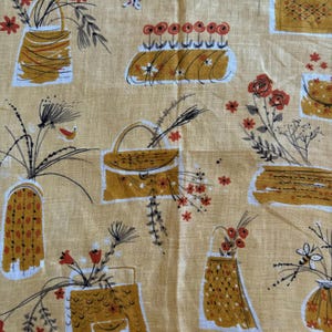 May include: A beige fabric with a repeating pattern of stylized baskets and flowers. The baskets are in shades of brown and yellow, and the flowers are red and white. The fabric has a linen-like texture.