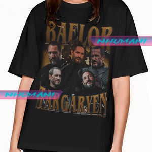 Könnte beinhalten: Schwarzes T-Shirt mit einem Grafikdesign im Vintage-Stil, das mehrere Männer zeigt, mit dem Text "BAELOR" darüber und "TARGARYEN" darunter. Die Grafik hat ein Gold- und Braunschema mit einem Used-Look.