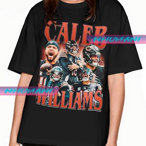 Può includere: T-shirt nero con grafica di una squadra di football, con la scritta "CALEB WILLIAMS" in arancione e bianco. Il design include immagini di giocatori con caschi e uniformi. La maglietta è un classico girocollo.