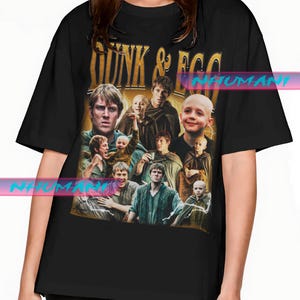 May include: Black t-shirt with a gold text reading "Dunk & Egg" above a collage of images. The images show people in medieval attire. The shirt has a crew neck and short sleeves.