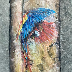 Pintura original de gran tamaño en técnica mixta sobre cartón grueso reciclado, hecho a mano y artesanalmente. Lista para enmarcar. Guacamayo sobre un muro de piedra antiguo.