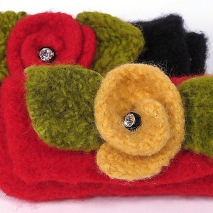 May include: Two knitted fabric wristlets with flower embellishments. The wristlets are red, black, and green with a yellow flower on one and a red flower on the other. Each flower has a rhinestone in the center.