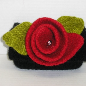 May include: A black felt rose with green felt leaves and a pink rhinestone in the center.