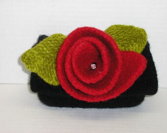 May include: A black felt rose with green felt leaves and a pink rhinestone in the centre.