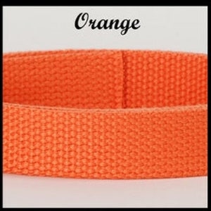 May include: A bright orange woven fabric strap with a distinct textured grid pattern. The word Orange is printed in a black cursive script font above the strap, which is positioned horizontally across the center of the frame.