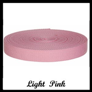 May include: A roll of light pink woven webbing tape featuring a consistent herringbone pattern throughout the material. The textile strip is coiled into a flat, circular shape with a smooth, uniform texture and edges, labeled with the text Light Pink.