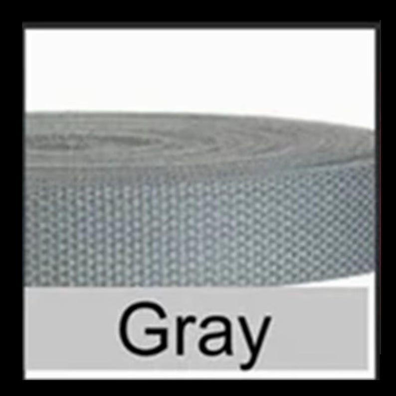 May include: A roll of gray webbing strap featuring a consistent woven texture. The material is wound into a circular coil, displaying a uniform light gray color throughout the entire length of the fabric strip. The word Gray is printed below.