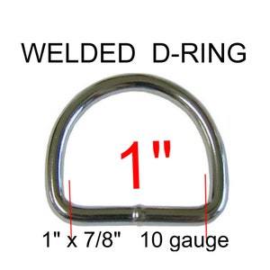 May include: A silver-colored metal welded D-ring with a smooth, reflective finish. The text WELDED D-RING is printed above the object. Red text indicates a 1 inch size, with additional text noting 1 inch by 7/8 inch dimensions and 10 gauge thickness.