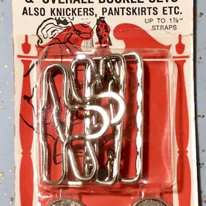 Puede incluir: Paquete vintage de Hot Pants & Overall Buckle Sets. El paquete incluye 2 botones, 2 hebillas y 2 deslizadores. El paquete es rojo y blanco con el texto "Hot Pants" y "USA" impreso.