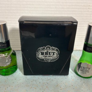 May include: A set of Brut for Men products, including two green glass bottles with silver caps and a black box. The bottles contain lotion and aftershave, with a silver label and chain detail. The box features the Brut logo.