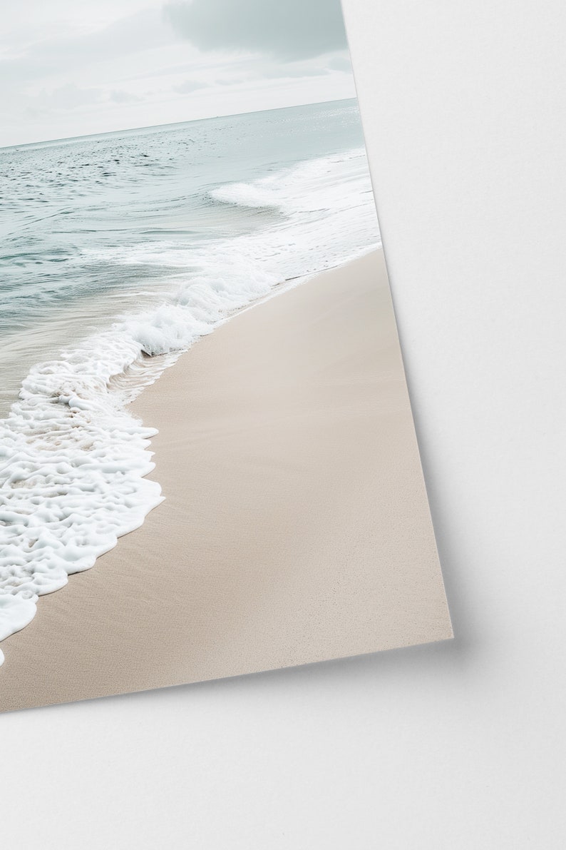May include: A tranquil beach vista featuring pale beige sand and calm waves. The sea shifts from a light turquoise to a deeper blue, with white foam from the breaking waves. The sky is overcast.