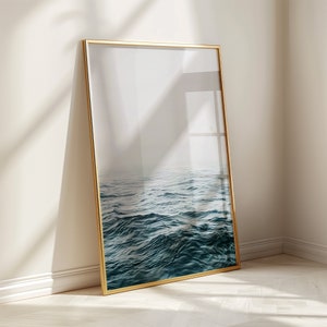 Könnte beinhalten: Ein gerahmtes Foto eines blauen Ozeans mit Wellen. Der Rahmen ist golden und das Foto ist im Hochformat.